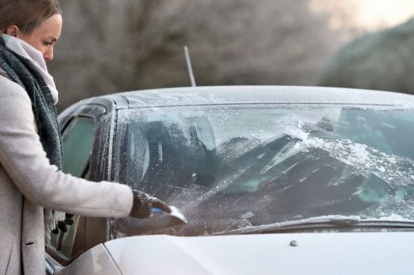 A woman scraping the ice off her car window
