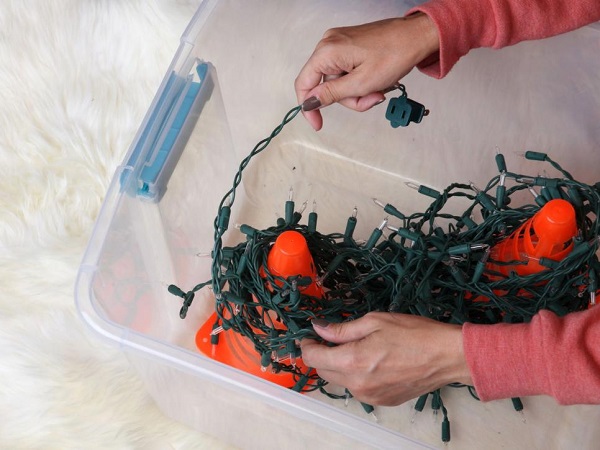 A person storing christmas lights in a storage box